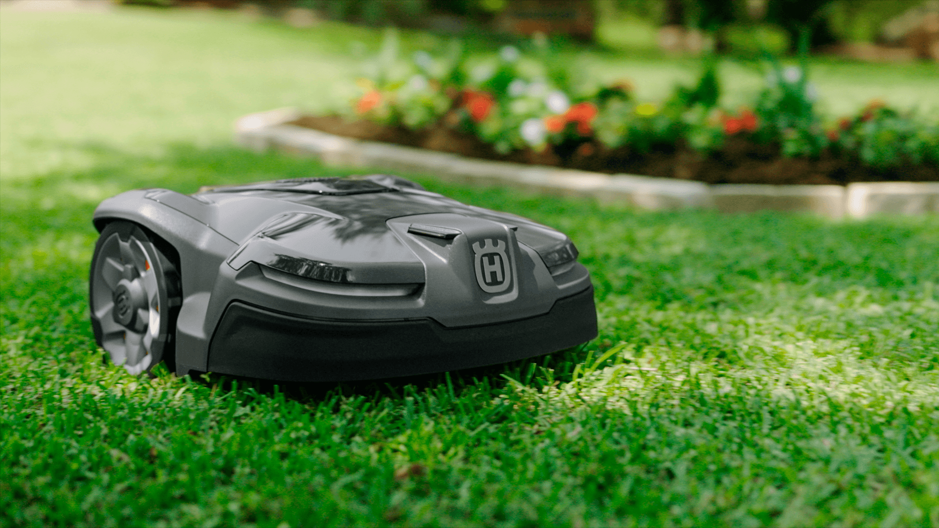 automower on green grass with garden bed behind